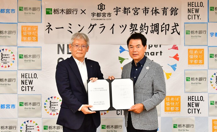 仲田取締役頭取と佐藤市長が契約書を持つ様子